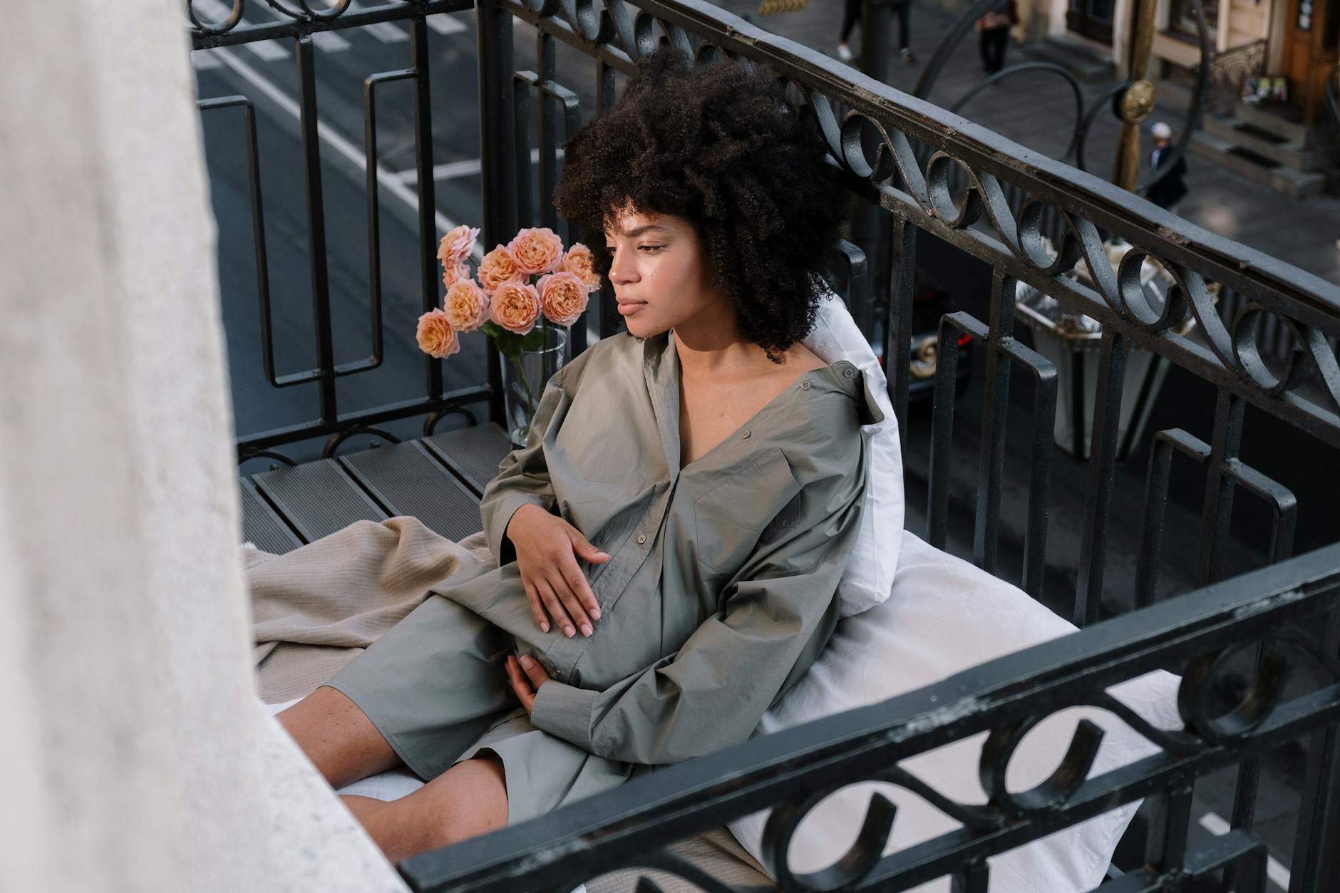 Kobieta w ciąży siedzi na balkonowym fotelu wśród kwiatów