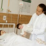 Lekarz pomaga świeżo upieczonej mamie z noworodkiem w sali szpitalnej