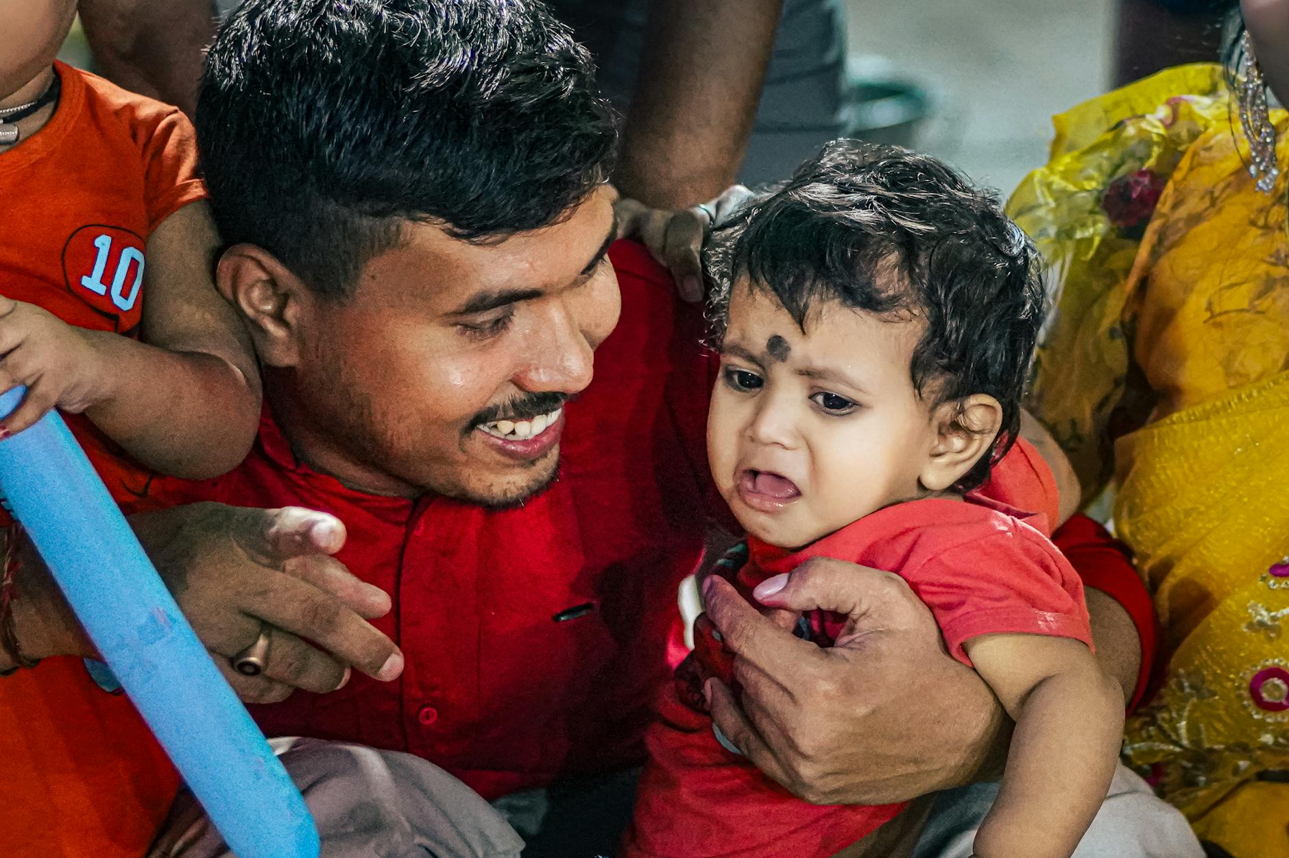 Tata przytula płaczące niemowlę na rodzinnym spotkaniu w domu