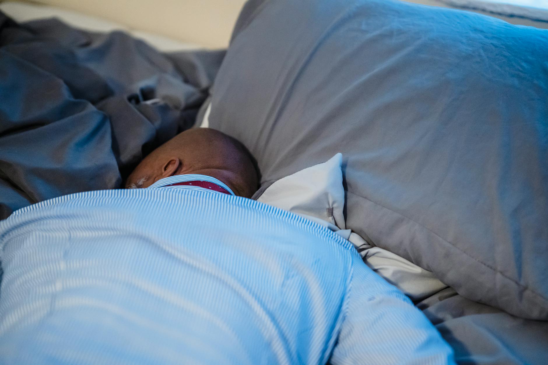 Dorosła osoba śpiąca spokojnie w łóżku z szarą pościelą