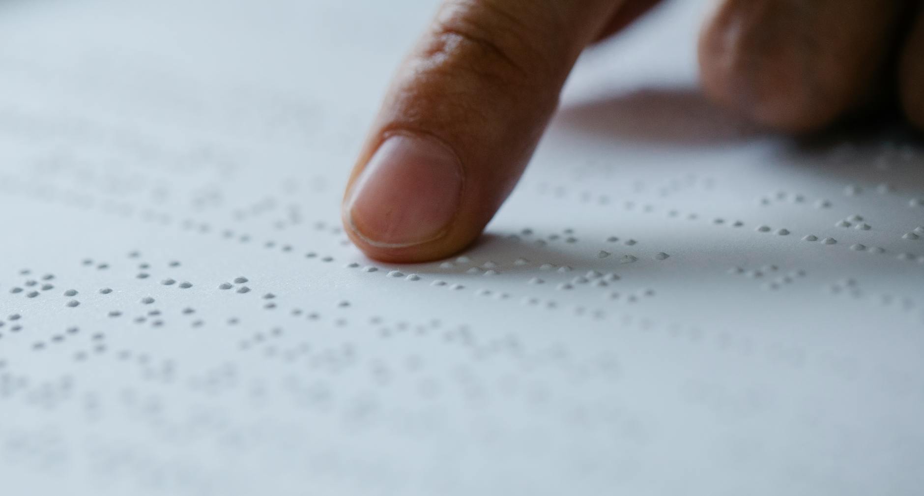 Palec przesuwający po wypukłych znakach pisma Braille’a na białej kartce