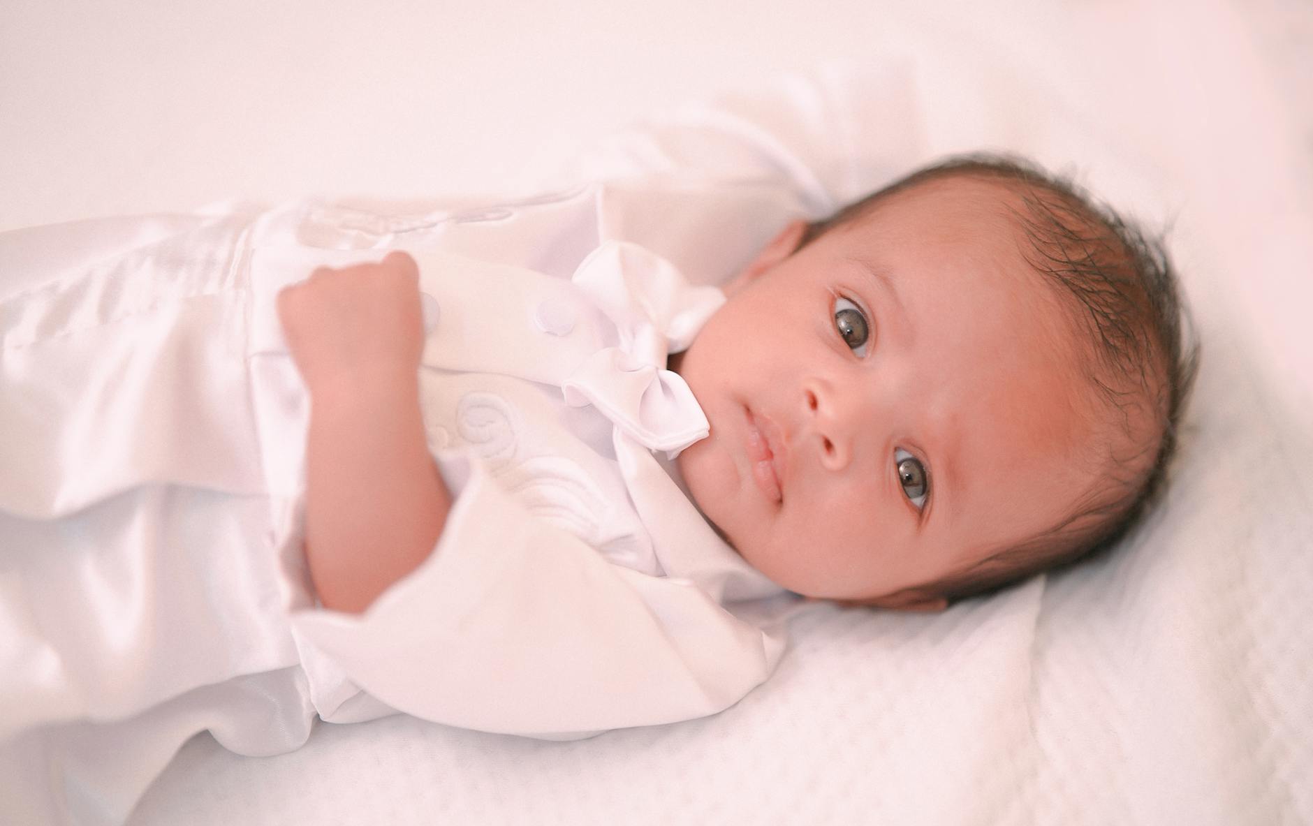 Śpiące niemowlę w białym ubranku leży spokojnie na miękkim łóżku