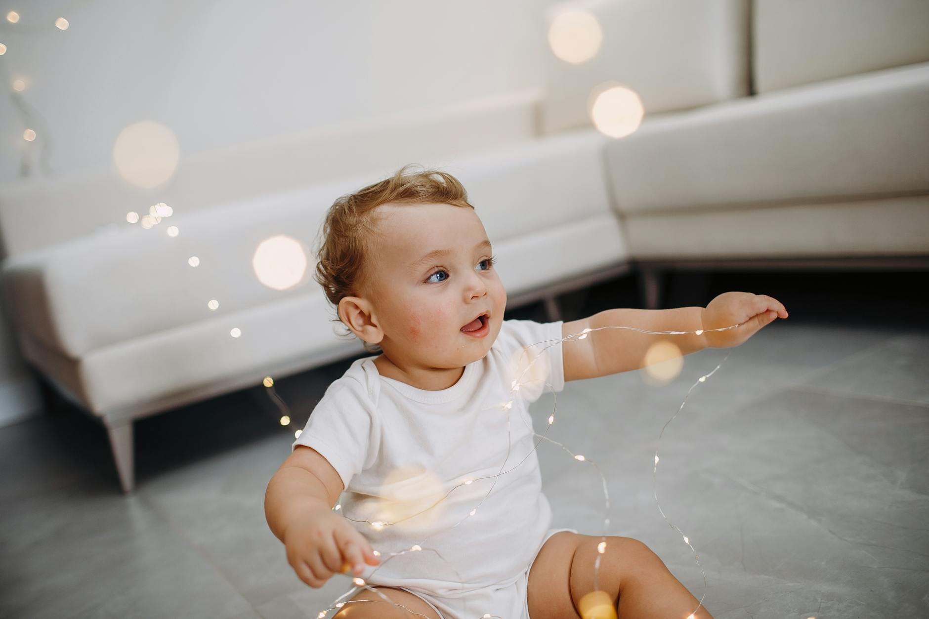 Niemowlę bawiące się światełkami na tle beżowej kanapy
