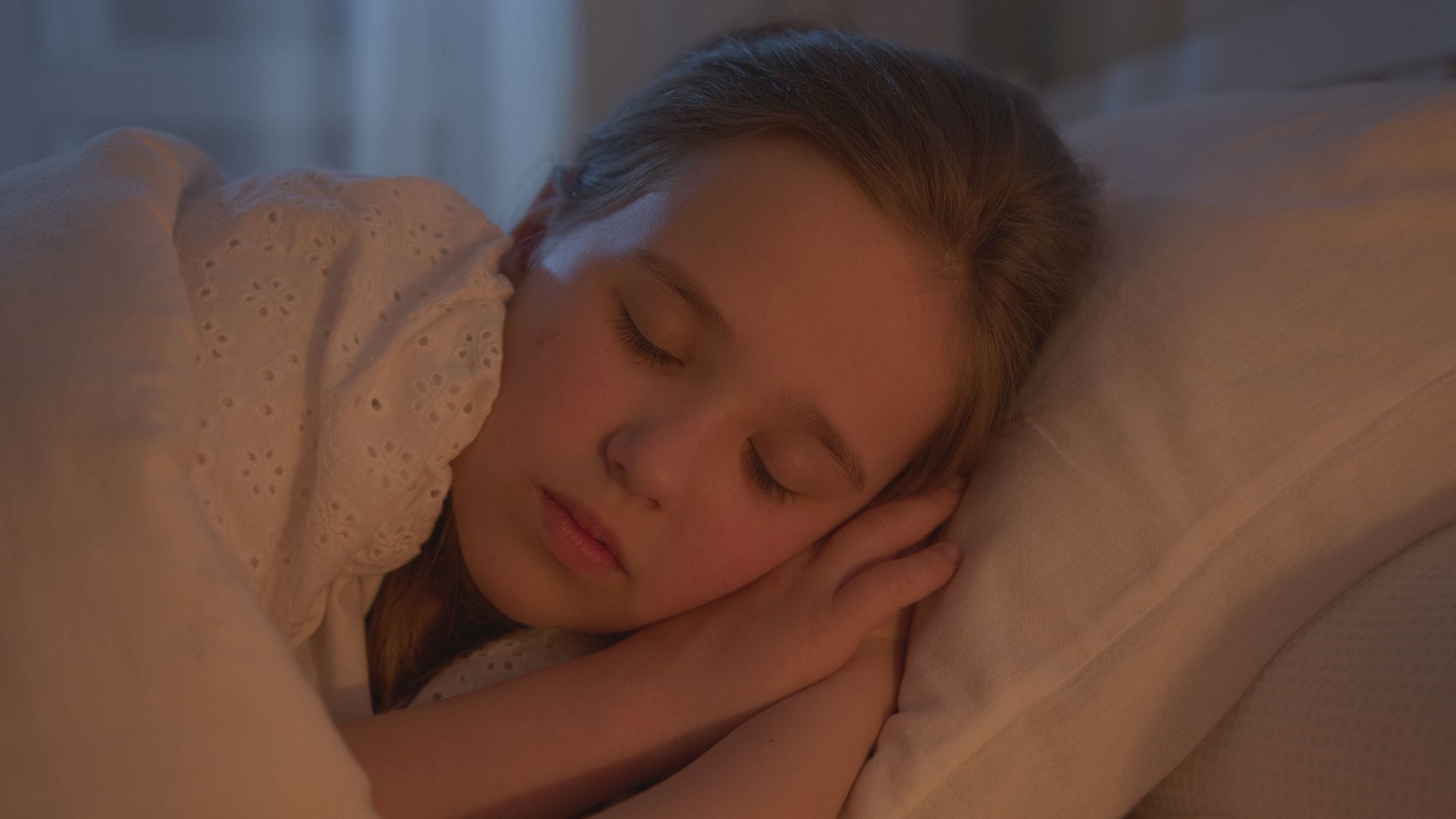 Śpiąca dziewczynka w łóżku w ciepłym świetle nocnej lampki