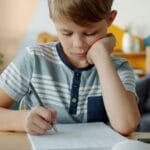 Prawidłowy chwyt kredki u 4-latka i 5-latka – proste ćwiczenia małej motoryki w domu Skupiony chłopiec odrabia pracę domową przy stole w domu