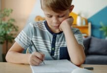 Prawidłowy chwyt kredki u 4-latka i 5-latka – proste ćwiczenia małej motoryki w domu Skupiony chłopiec odrabia pracę domową przy stole w domu